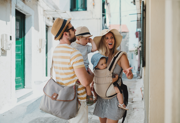 Famille en vacances d’été avec bébé en porte-bébé et enfant lors d’une balade en ville