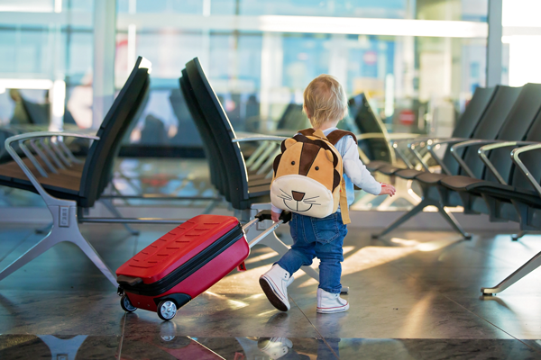Enfant avec sac à dos et valise cabine dans un aéroport avant un voyage en famille