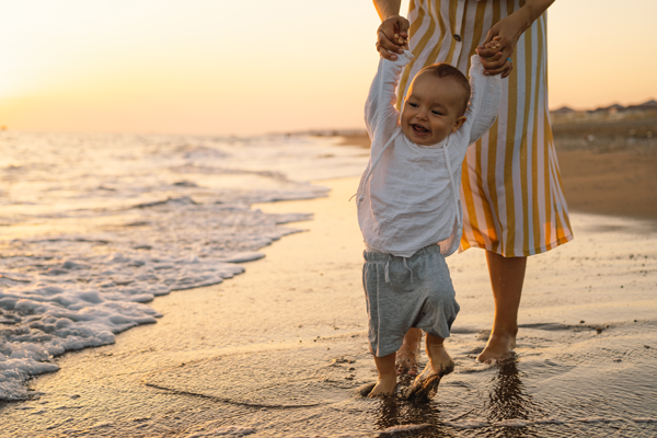 Bébé marchant sur la plage en été pendant des vacances en famille au bord de la mer