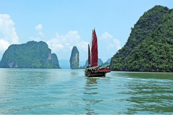 Jonque traditionnelle à voiles rouges naviguant au milieu des îlots karstiques de la baie d’Ha Long, au Vietnam.